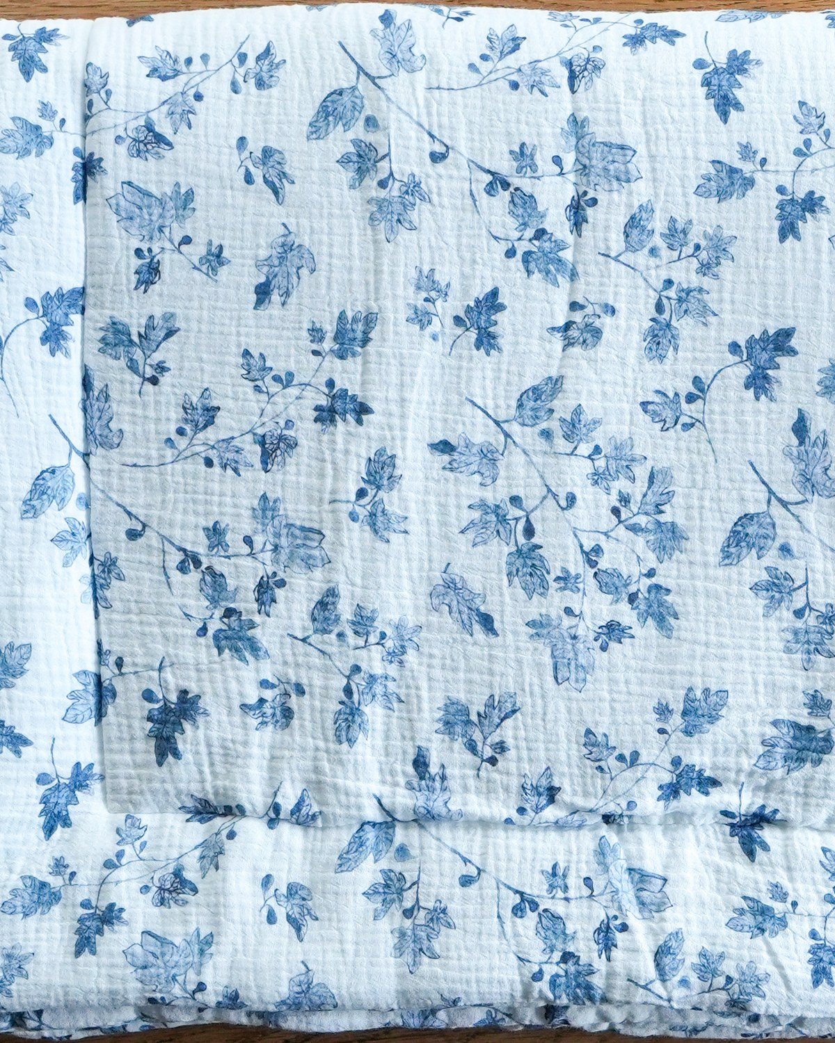 Fig muslin playmat folded on an oak table