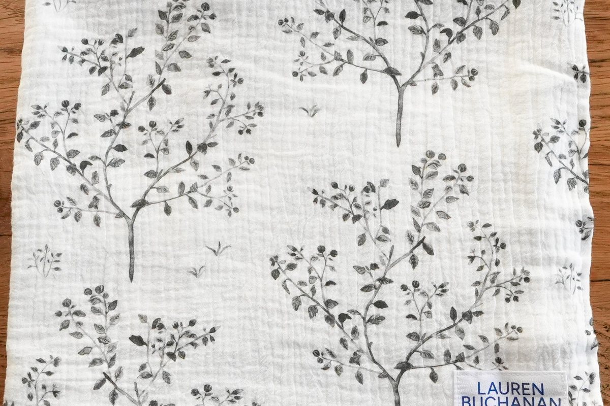 Muslin swaddle blanket in Snowberry, folded, with grey snowberry branches painted on white cloth
