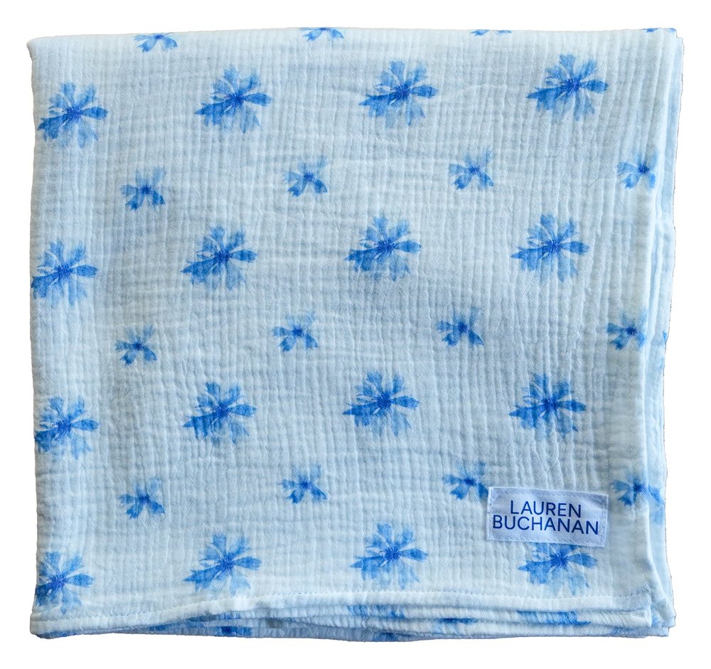 Muslin swaddle blanket in Cornflower, folded, with scattered blue cornflower heads on white cloth